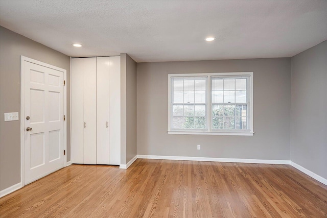 unfurnished bedroom featuring light wood-type flooring, baseboards, a textured ceiling, and a closet