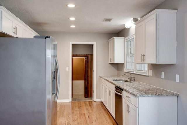 kitchen with white cabinets, appliances with stainless steel finishes, light wood-style floors, and a sink