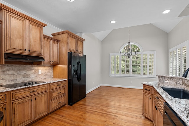 kitchen with light stone countertops, vaulted ceiling, sink, black appliances, and a notable chandelier