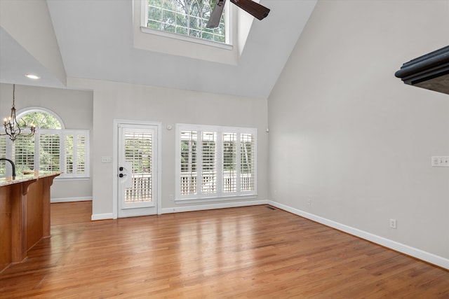 unfurnished living room featuring ceiling fan with notable chandelier, a high ceiling, and light hardwood / wood-style flooring