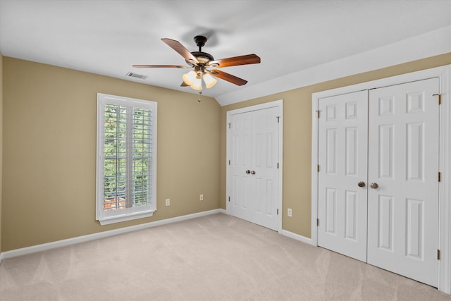 unfurnished bedroom featuring ceiling fan, lofted ceiling, light carpet, and multiple closets