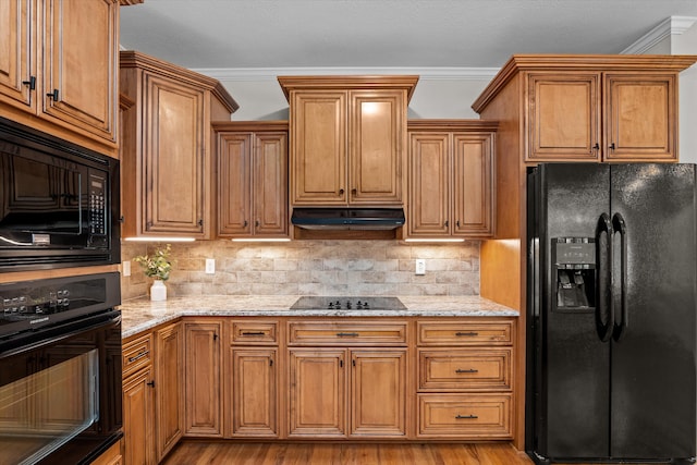 kitchen with backsplash, light stone counters, ornamental molding, black appliances, and light hardwood / wood-style floors