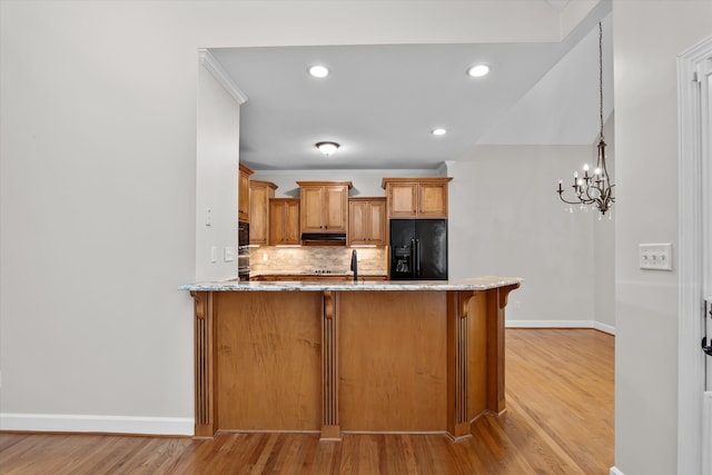 kitchen featuring kitchen peninsula, tasteful backsplash, black appliances, light hardwood / wood-style flooring, and a chandelier