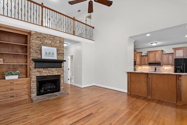 living room featuring light hardwood / wood-style floors, built in features, ceiling fan, and a stone fireplace