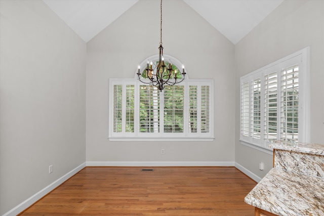 unfurnished dining area featuring hardwood / wood-style flooring, high vaulted ceiling, and an inviting chandelier