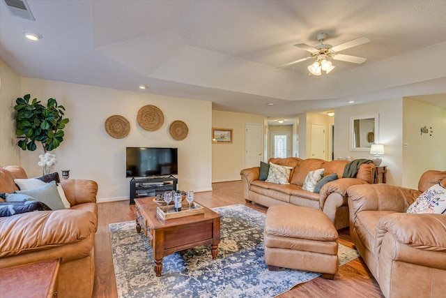 living room with light hardwood / wood-style flooring, a raised ceiling, and ceiling fan