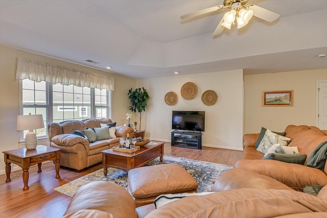 living room featuring a tray ceiling, ceiling fan, and light hardwood / wood-style floors