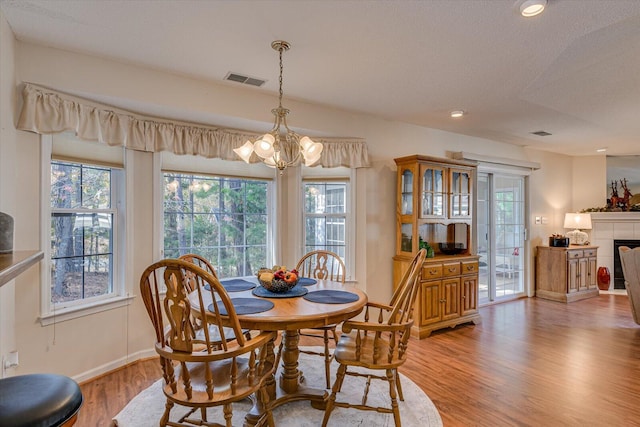 dining space featuring a textured ceiling, light hardwood / wood-style floors, a fireplace, and a chandelier