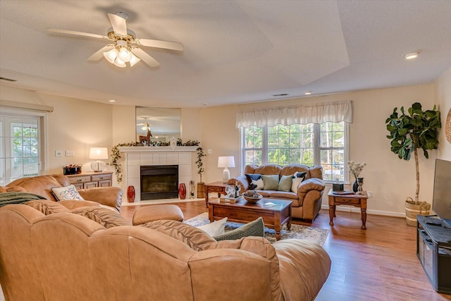 living room featuring wood-type flooring, a raised ceiling, ceiling fan, and a tiled fireplace