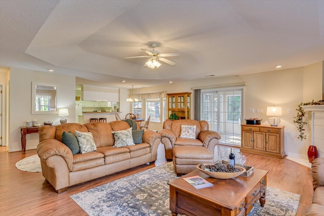 living room with ceiling fan with notable chandelier, a tray ceiling, and light hardwood / wood-style floors