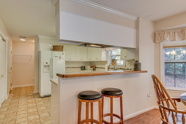 kitchen with a kitchen breakfast bar, kitchen peninsula, white cabinets, and white refrigerator with ice dispenser