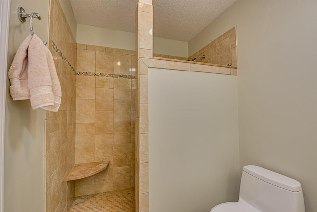 bathroom with a textured ceiling, toilet, and tiled shower