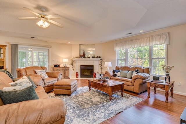 living room with hardwood / wood-style flooring, ceiling fan, and a tiled fireplace