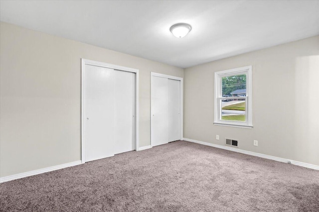 unfurnished bedroom featuring carpet and two closets