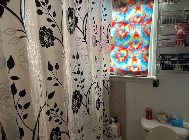 bathroom featuring curtained shower, tile walls, and toilet