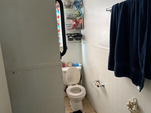 bathroom featuring tile patterned flooring, wainscoting, toilet, and tile walls