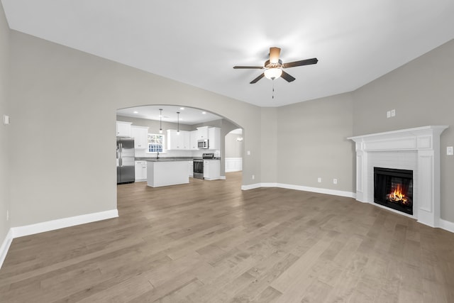 2767 Huntcliffe Dr, Augusta, GA 30909 - unfurnished living room with baseboards, light wood-type flooring, a ceiling fan, a brick fireplace, and arched walkways