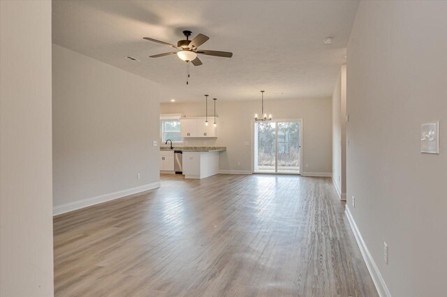 unfurnished living room featuring ceiling fan with notable chandelier and light wood-type flooring