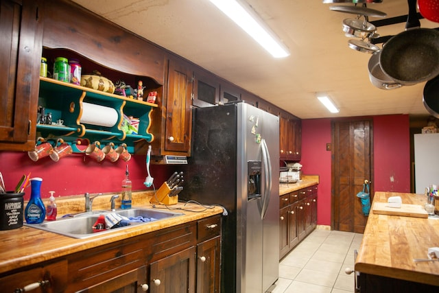 kitchen with light tile patterned flooring, stainless steel fridge, butcher block counters, and sink