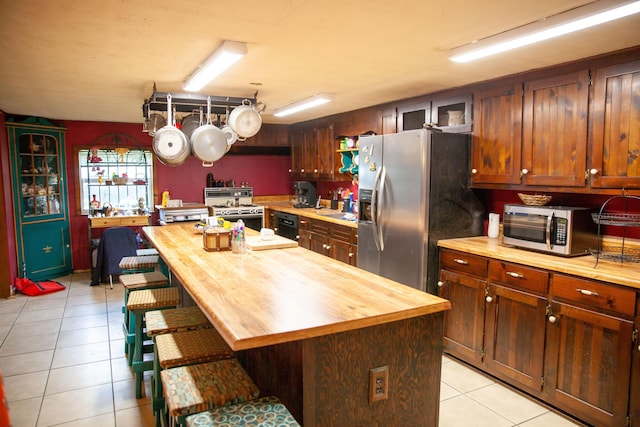 kitchen featuring light tile patterned floors, wooden counters, a breakfast bar, a kitchen island, and appliances with stainless steel finishes