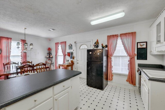 kitchen with pendant lighting, black refrigerator, white cabinetry, and a textured ceiling