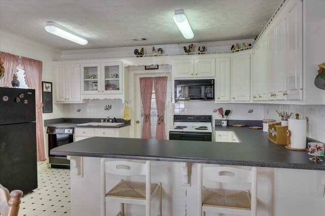 kitchen featuring a kitchen bar, kitchen peninsula, white cabinetry, and black appliances