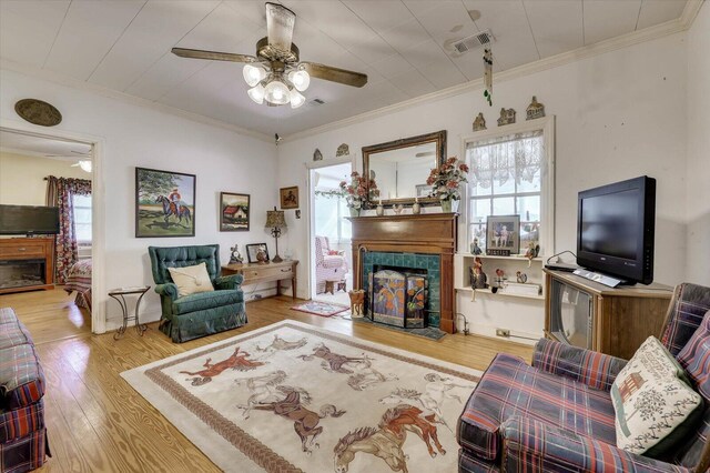 living room with a tiled fireplace, ceiling fan, light hardwood / wood-style floors, and ornamental molding