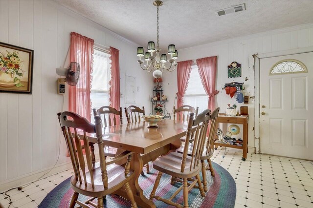 dining space with a textured ceiling, crown molding, a notable chandelier, and wood walls