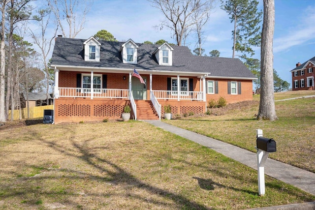 view of front of home with covered porch, brick siding, a front lawn, and a shingled roof