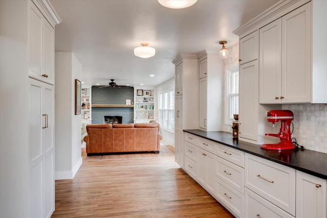 kitchen featuring light wood finished floors, a ceiling fan, dark countertops, open floor plan, and a fireplace