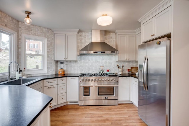 kitchen featuring stainless steel appliances, dark countertops, a sink, and wall chimney exhaust hood