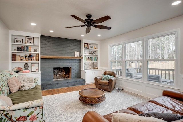 living area with built in features, wood finished floors, a brick fireplace, a decorative wall, and recessed lighting