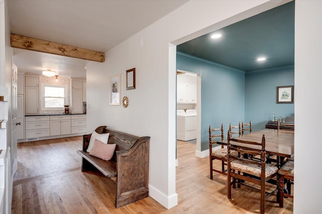 dining area featuring light wood finished floors, washing machine and clothes dryer, ornamental molding, beamed ceiling, and baseboards