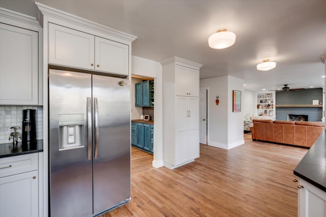 kitchen with stainless steel fridge, dark countertops, light wood-style flooring, open floor plan, and a fireplace