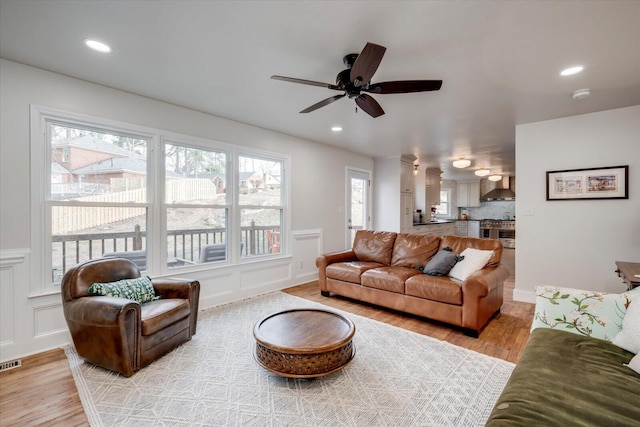 living room featuring light wood-style flooring, visible vents, a decorative wall, and recessed lighting