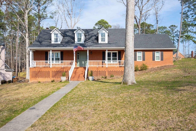 new england style home with covered porch, a shingled roof, a front lawn, and brick siding