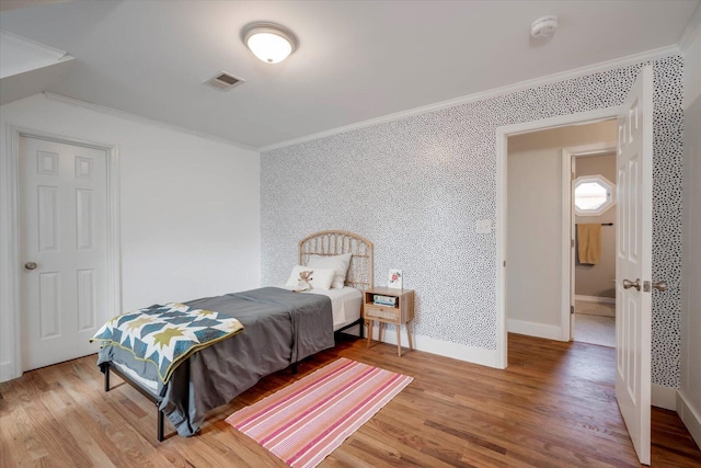 bedroom with baseboards, visible vents, ornamental molding, and wood finished floors