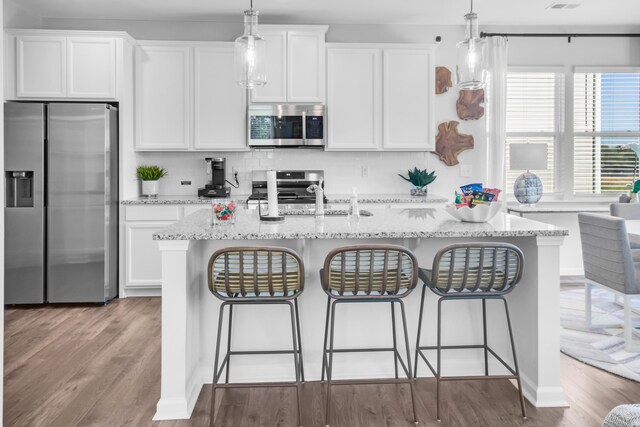 kitchen featuring a center island with sink, stainless steel appliances, white cabinets, wood finished floors, and a kitchen bar