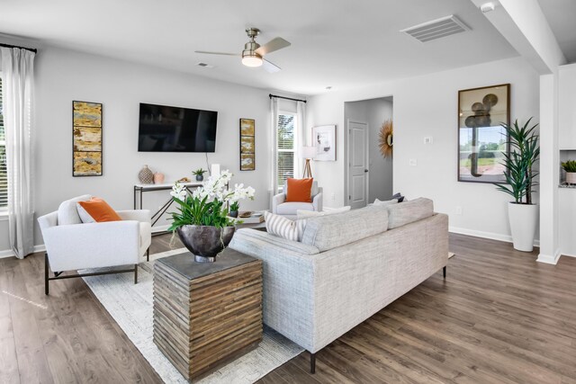 living area featuring a ceiling fan, visible vents, baseboards, and wood finished floors