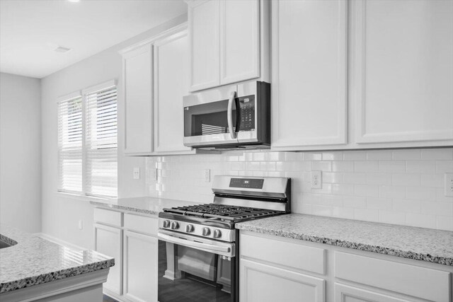 kitchen with light stone counters, white cabinetry, stainless steel appliances, and decorative backsplash