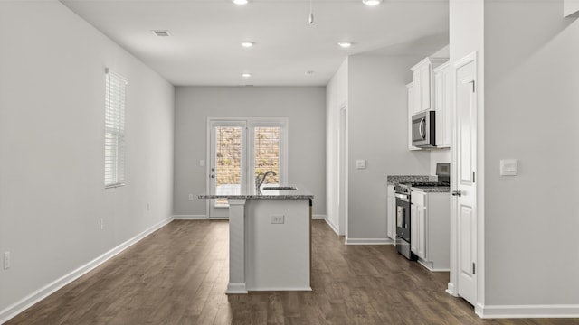 kitchen featuring light stone countertops, dark wood finished floors, a sink, appliances with stainless steel finishes, and white cabinetry