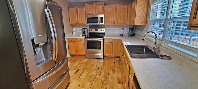 kitchen featuring crown molding, sink, light wood-type flooring, appliances with stainless steel finishes, and tasteful backsplash