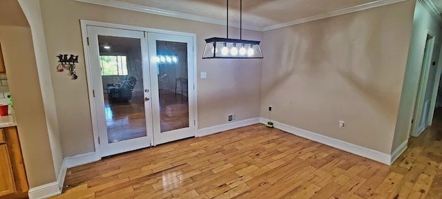 unfurnished dining area featuring crown molding, french doors, and light wood-type flooring