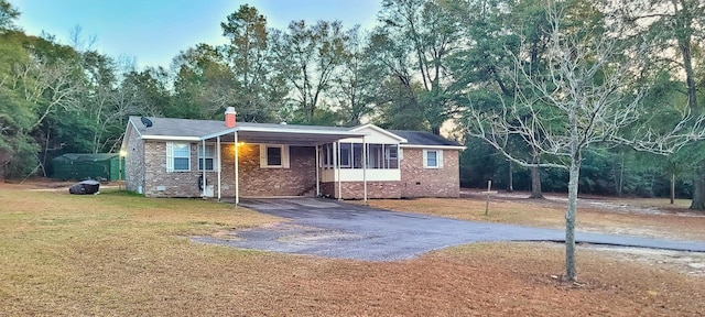 single story home with a front lawn, a carport, and a sunroom