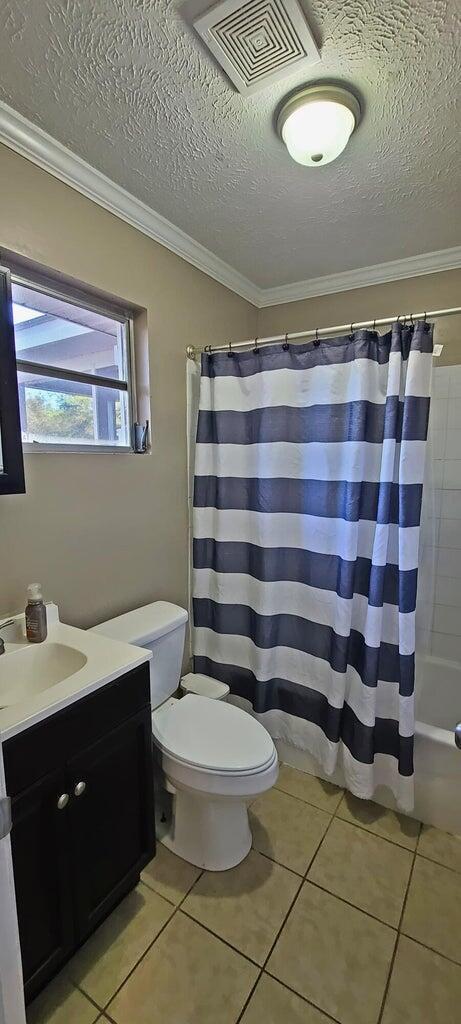 full bathroom featuring vanity, tile patterned floors, toilet, ornamental molding, and shower / bathtub combination with curtain