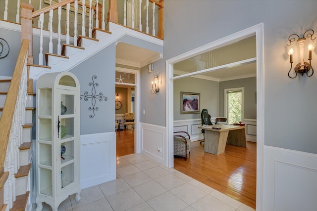 entrance foyer featuring a decorative wall, a wainscoted wall, light wood-style floors, stairs, and ornamental molding