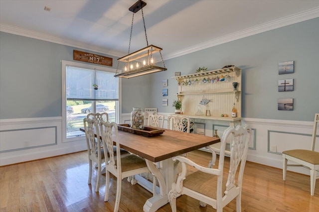 dining room with light wood-style floors, crown molding, and a wainscoted wall