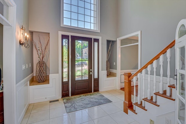 foyer entrance featuring stairs, wainscoting, light tile patterned flooring, and a decorative wall