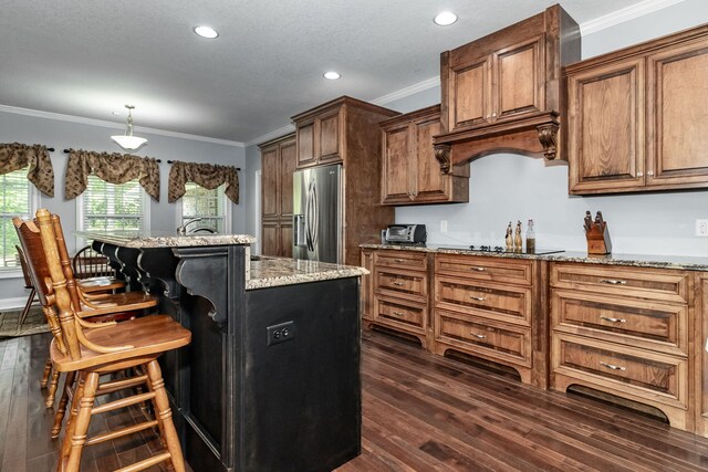 kitchen with a kitchen bar, light stone countertops, ornamental molding, stainless steel fridge with ice dispenser, and a center island