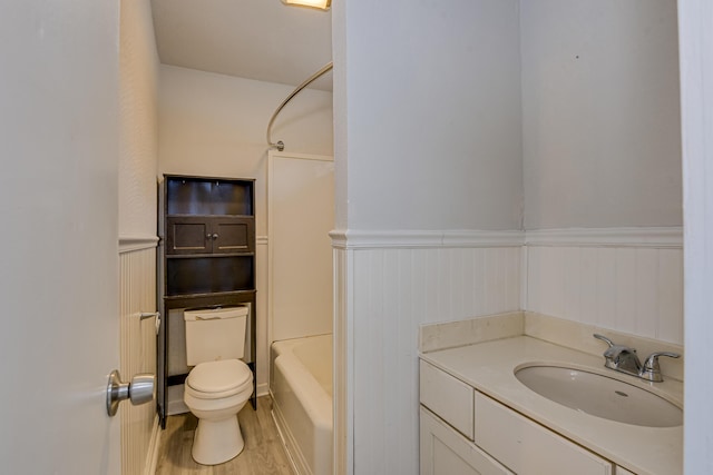 bathroom with vanity, wood finished floors, wainscoting, shower / bath combination, and toilet